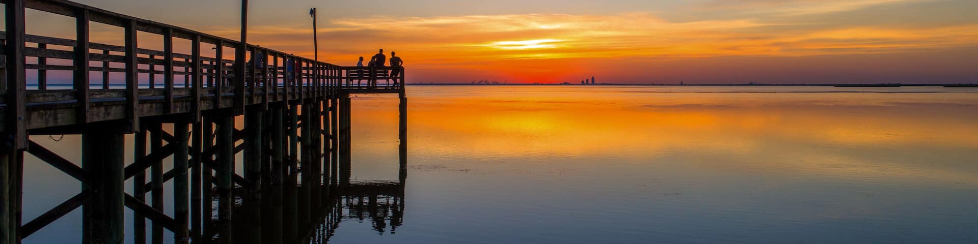 A pier extending into calm waters at sunset with a clear sky.