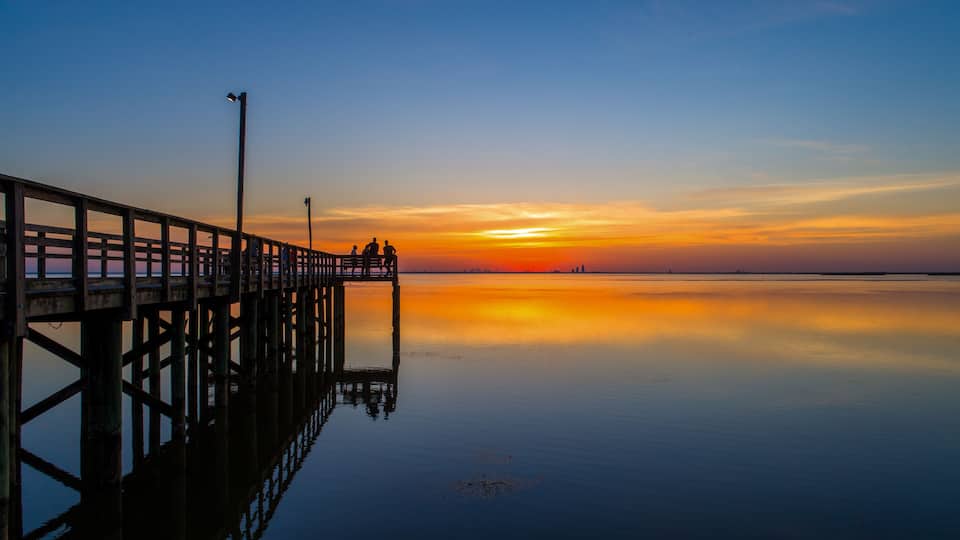 A pier extending into calm waters at sunset with a clear sky.