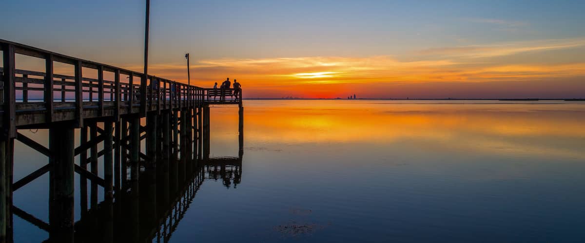 A pier extending into calm waters at sunset with a clear sky.