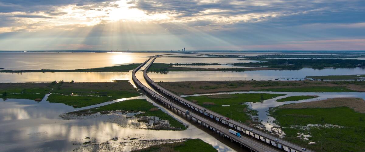A highway curving through a coastal landscape with a sunset in the background.
