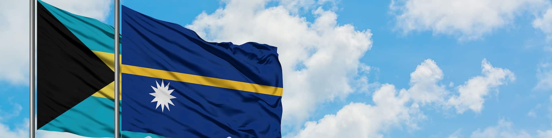 Bahamas and Nauru flag waving in the wind against white cloudy blue sky together. Diplomacy concept, international relations.