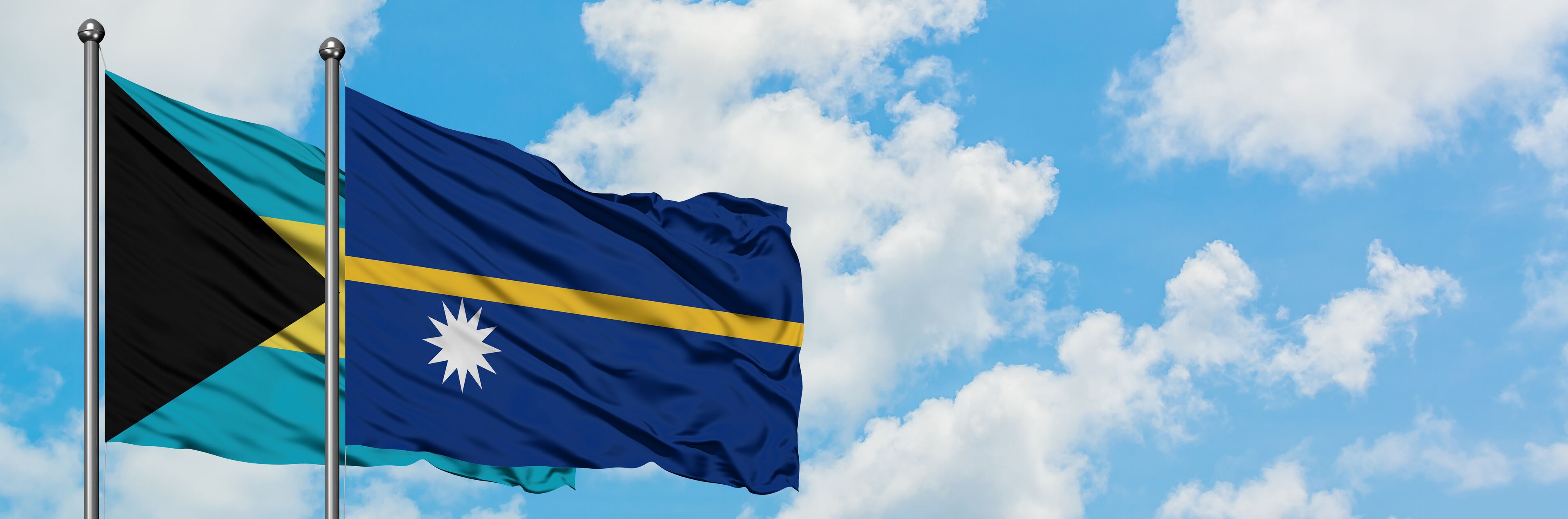Two flags waving against a blue sky with clouds.