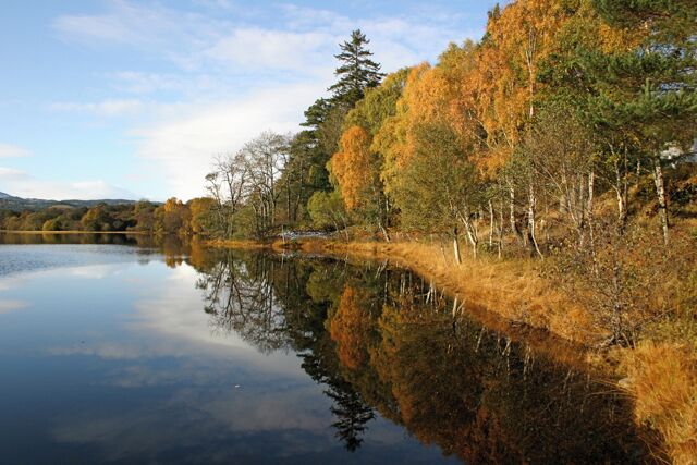 A calm lake with autumn-colored trees reflecting on the water.