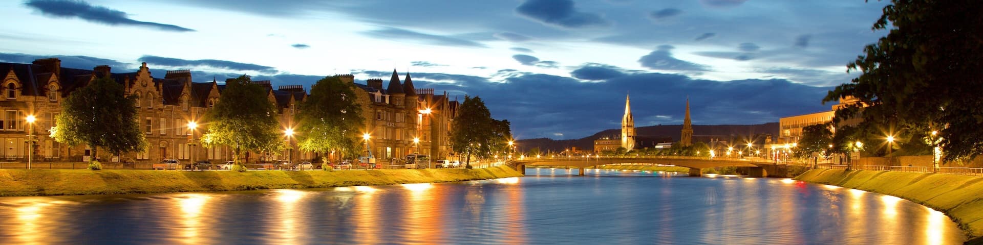 A river with a bridge, historic buildings, and a church tower at dusk.