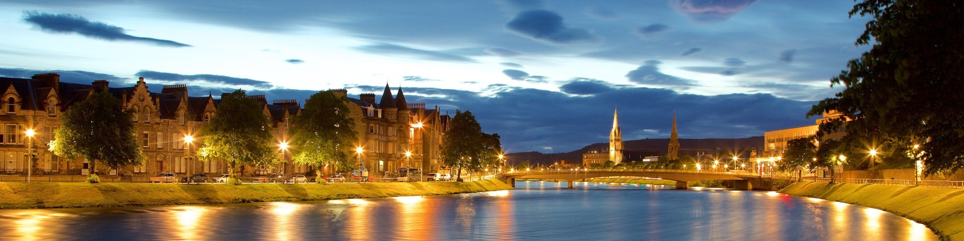 A river with a bridge, historic buildings, and a church tower at dusk.