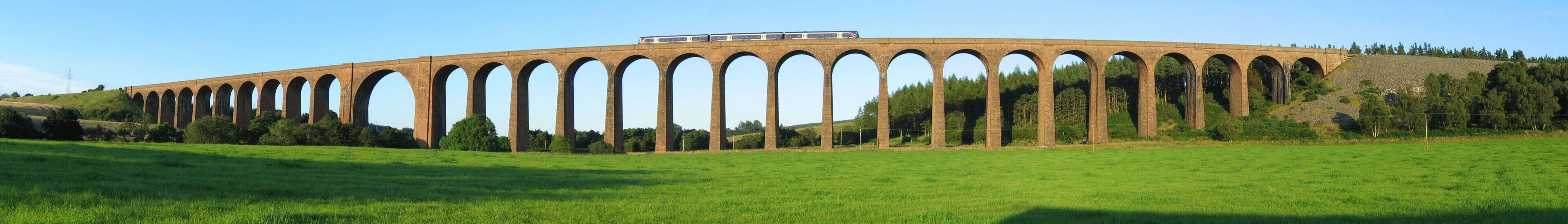 A viaduct with multiple arches over a green field.