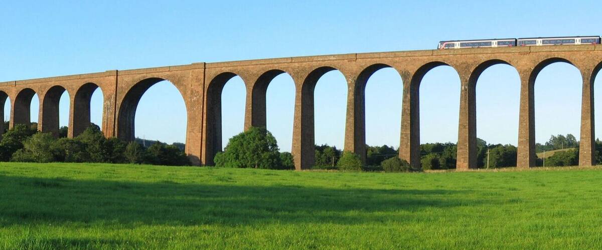A viaduct with multiple arches over a green field.