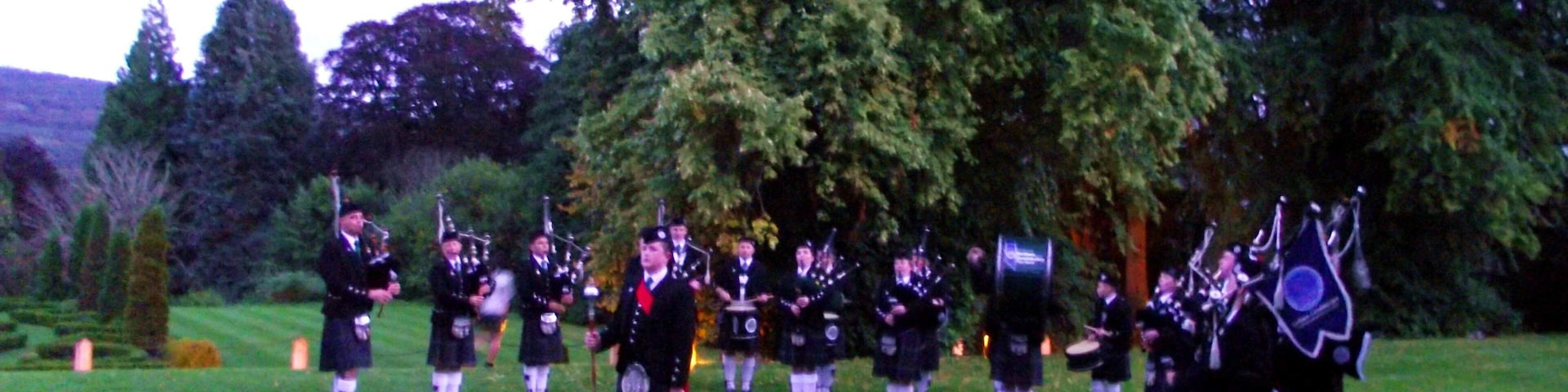 Band forms a semi circle on the lawn in front of the Castle in twilight. BAND AT ACHNAGAIRN CASTLE - The band were delighted to be asked to perform at the International Social Travel Summit Gala Dinner tonight at the beautiful Achnagairn Castle near inverness. The summit was attended by over 120 delegates from a considerable number of countries, and we were more than happy to entertain them outside this historic and beautiful building. Our slot was between the delegates arrival and their going into dinner. Pipe Major Steve Spencer was playing out on the front lawn in the gloaming - and the guests lapped up the "solo piper" performance - only for them to whoop with delight when the surprise appeared, the full Band marching out from the side of the Castle to join the Pipie on the lawn. Despite work and health issues at short notice, which saw the number of pipers diminished somewhat, we were still able to field ELEVEN pipers, SEVEN snare drummer, a bass and a Drum Major (20 in total). The delegates were obviously enjoying the performance when, all too soon, it was time for the Band to conclude and march off, so the guests could go to dine. Despite the failing light, hopefully my photographs will give a hint of the occasion - being an international event, VisitScotland anticipate many far better photos than mine all over the internet before long!