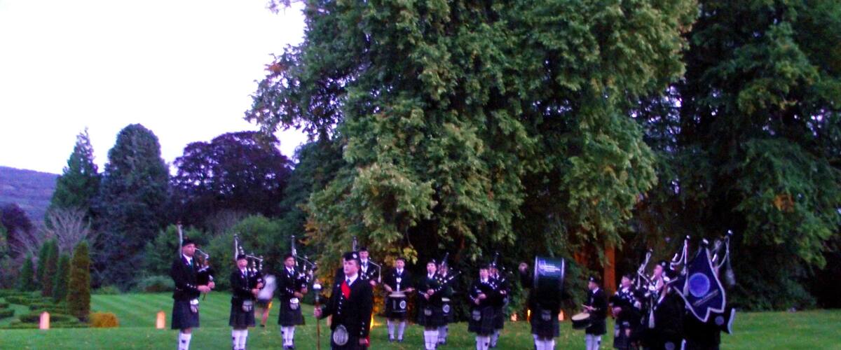 A group of bagpipers in kilts on a grassy field with trees in the background.