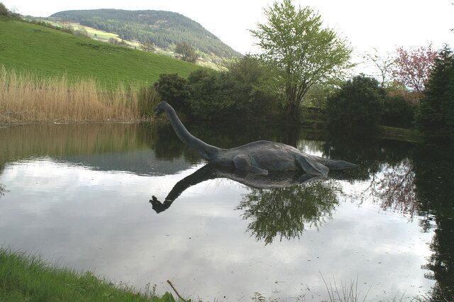 A sculpture of a bird in a pond with a grassy hill and trees in the background.