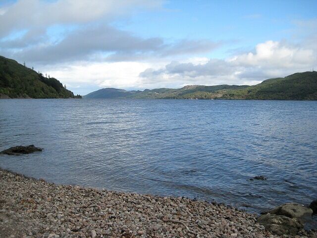 A calm lake with a rocky shoreline and hills in the background.