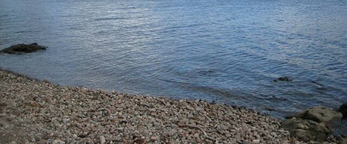 A calm lake with a rocky shoreline and hills in the background.