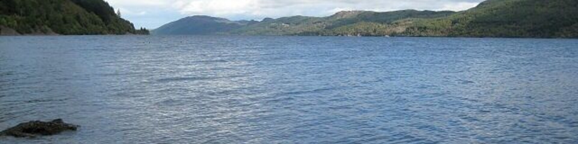 A calm lake with a rocky shoreline and hills in the background.