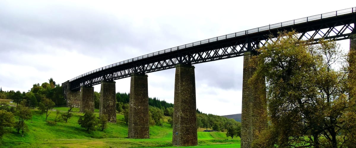 A large stone bridge spanning a river, surrounded by lush green hills and trees.