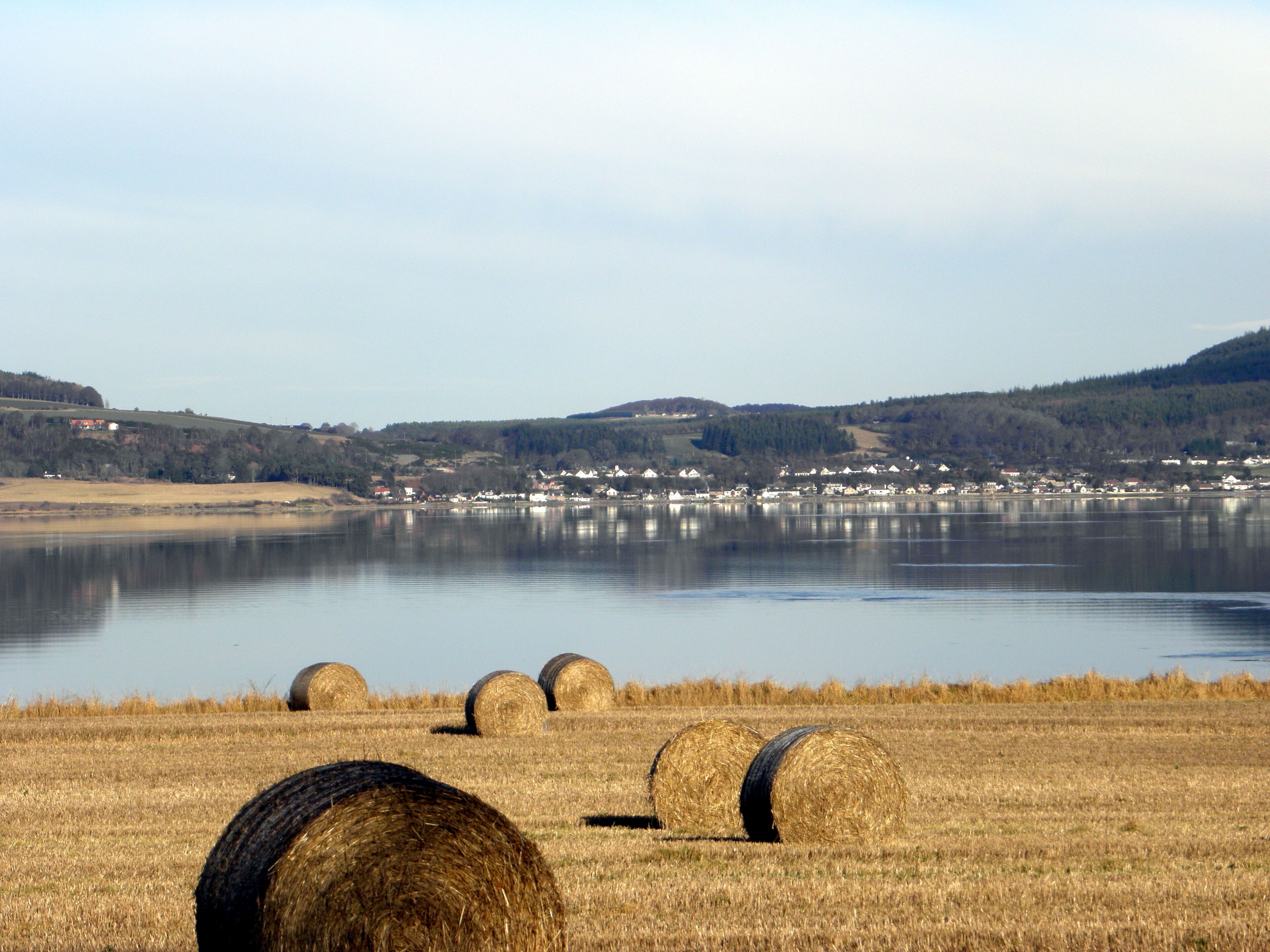 A lake with hay bales in the foreground and a town across the water.