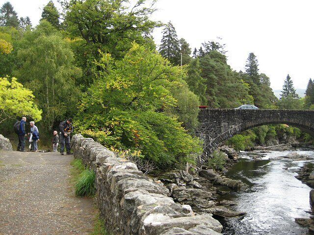 A stone bridge over a river, surrounded by trees and a stone wall.
