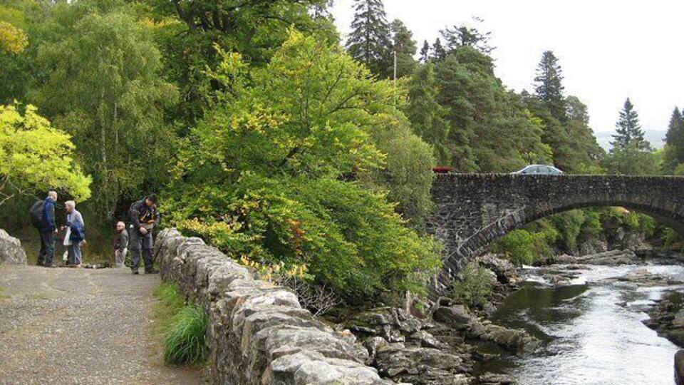 A stone bridge over a river, surrounded by trees and a stone wall.