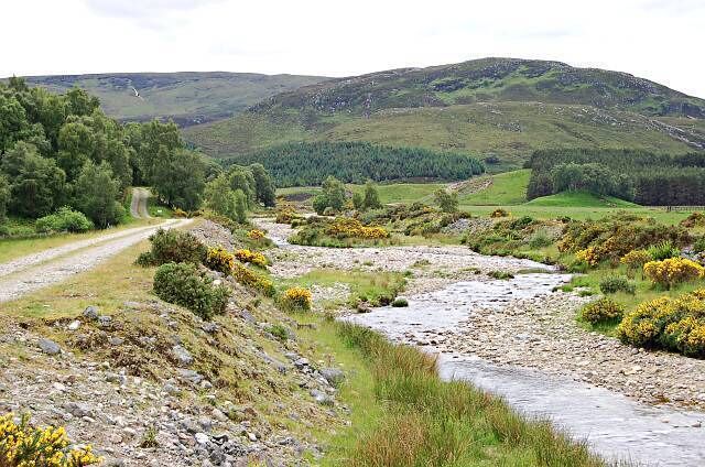 A rural landscape with a winding stream, grassy fields, and rolling hills.