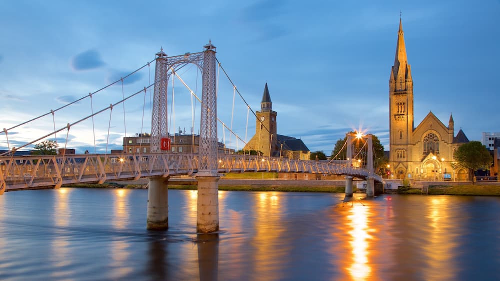 Un pont enjambant une rivière, avec une église et une tour en arrière-plan.