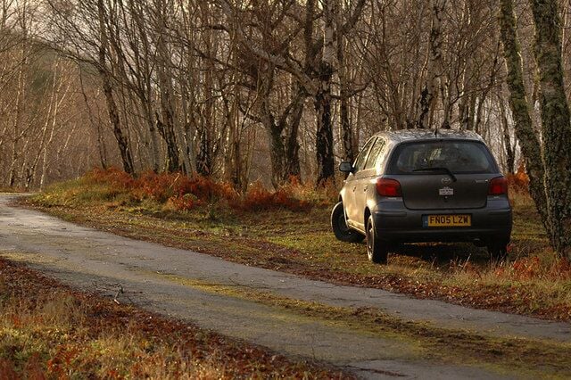 Um carro estacionado em uma estrada rural, cercado por árvores sem folhas.