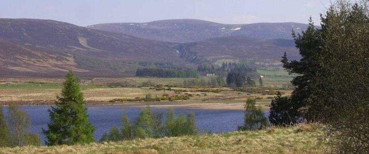 A lake surrounded by hills and sparse vegetation.