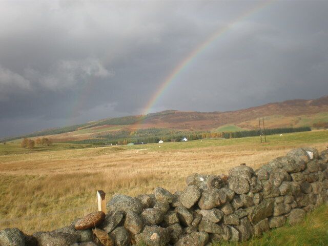 A stone wall, a grassy field, and a rainbow in a rural landscape.