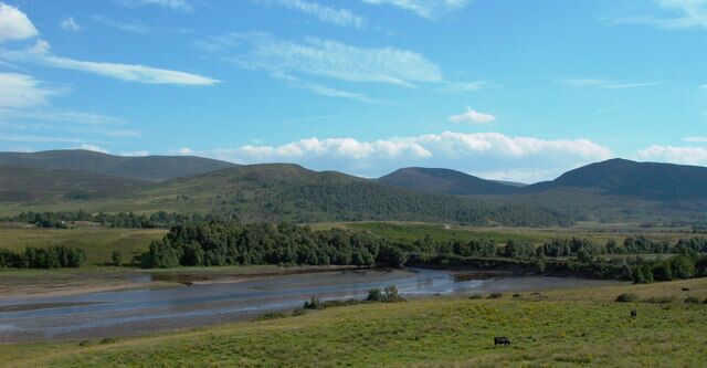 A river flowing through a grassy valley with hills in the background.
