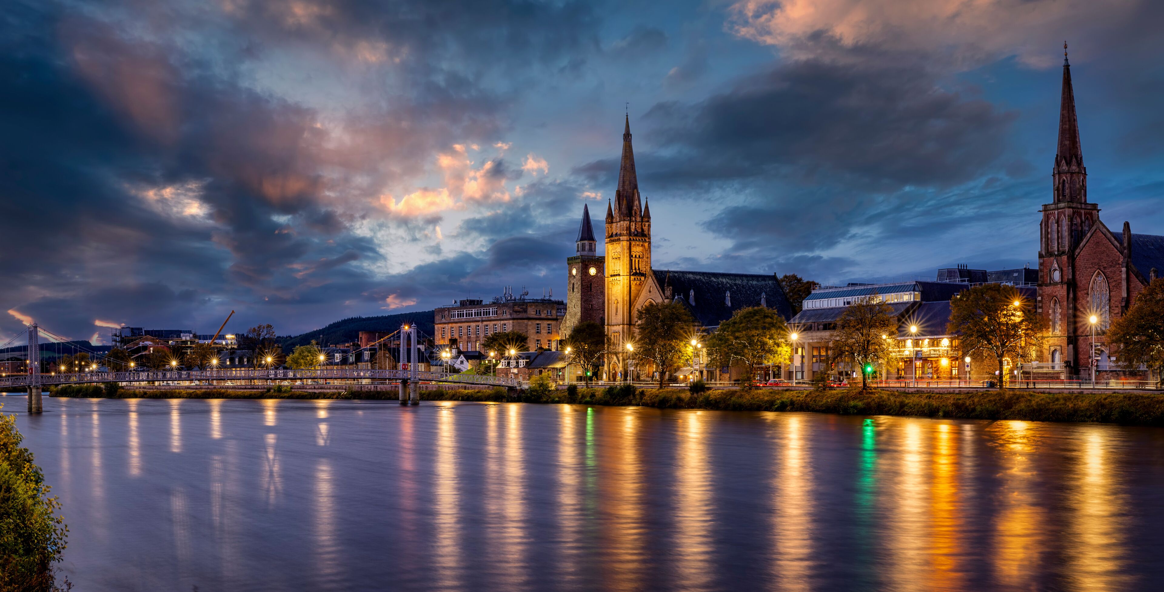 A river with a bridge, a church with a tall spire, and a building with a clock tower.