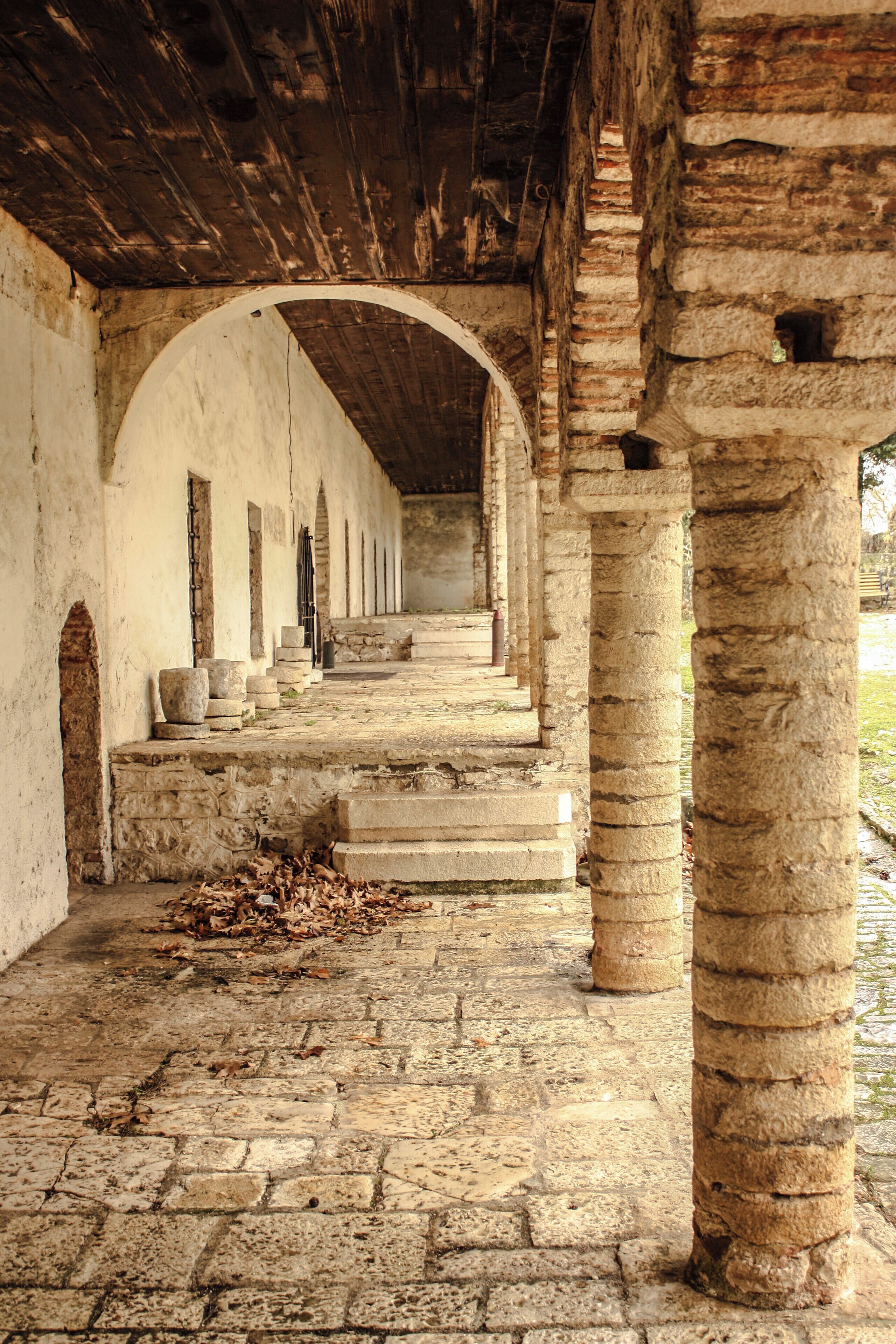 An ancient stone corridor with arches and columns, leading to a covered area.