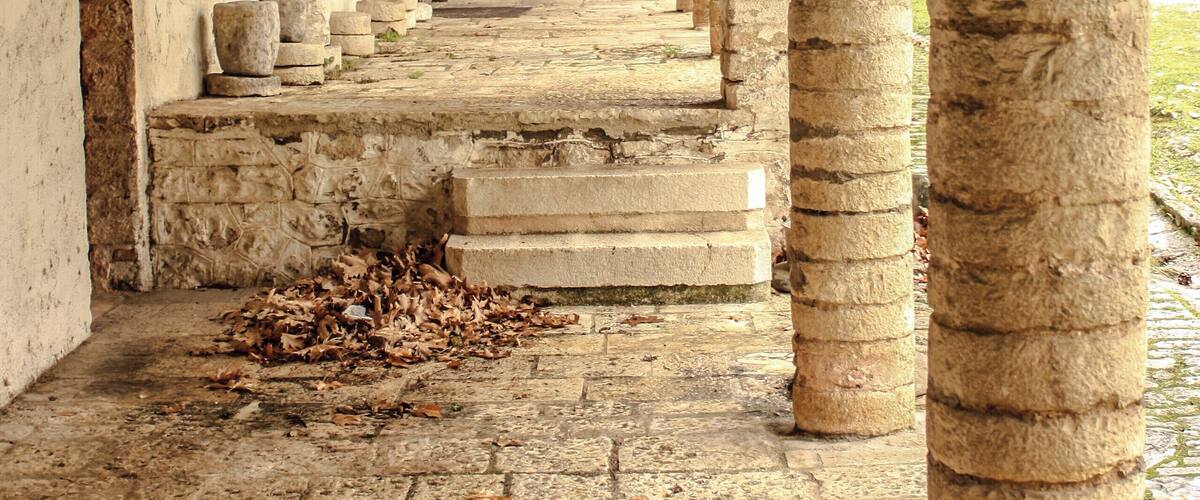 An ancient stone corridor with arches and columns, leading to a covered area.