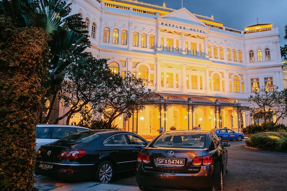 A grand hotel with classical architecture, parked cars, and lush greenery.