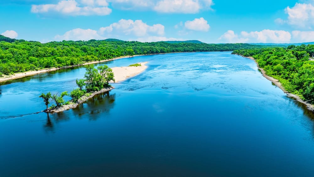 Une rivière bordée d’une végétation luxuriante, sous un ciel bleu clair.
