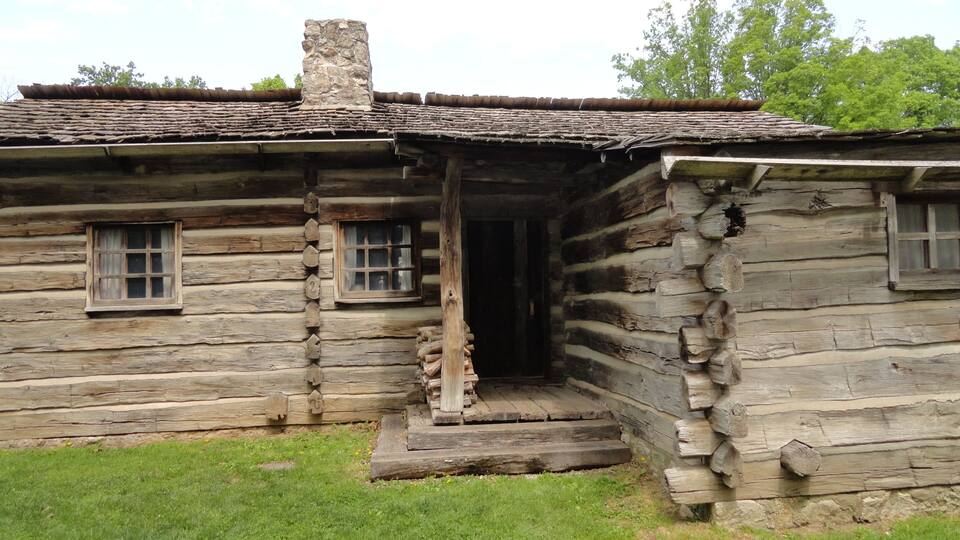 A rustic log cabin with a chimney, a porch, and a window.