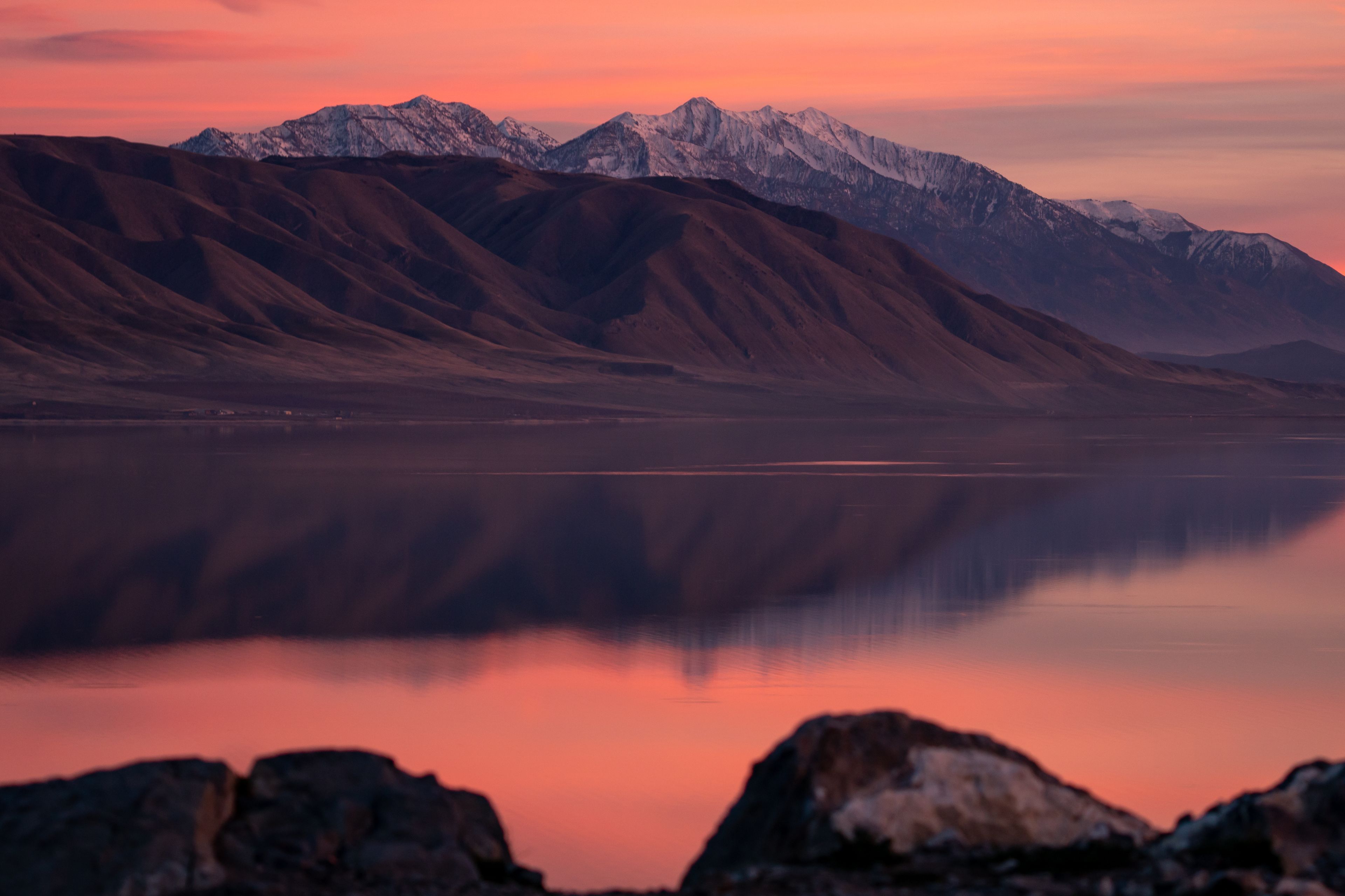 A mountain range with snow-capped peaks and a calm lake reflecting the sky.