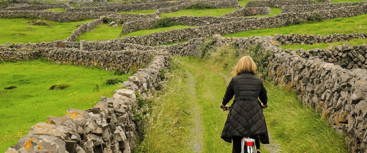 A person riding a bicycle on a stone path surrounded by grassy fields and stone walls.
