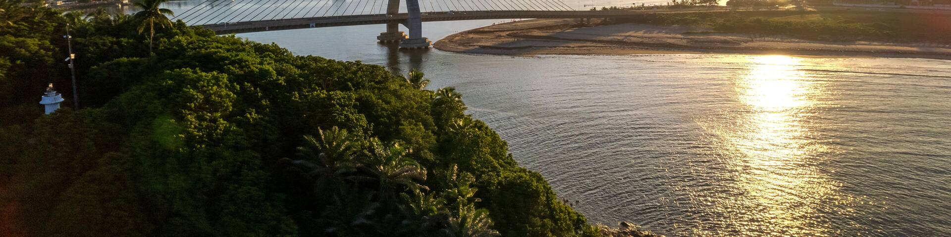 A cable-stayed bridge over a river with a sunset in the background.