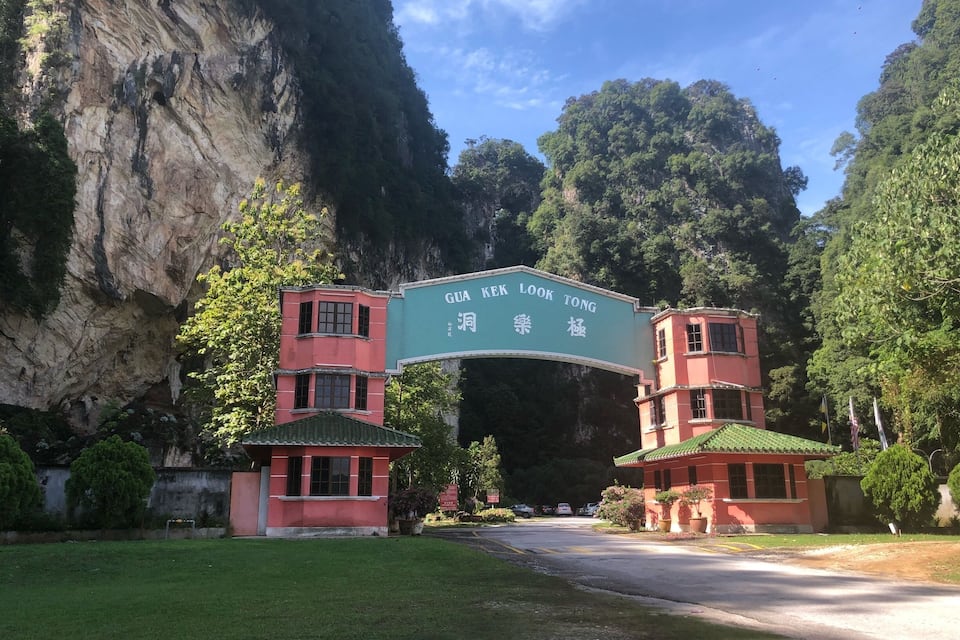 Una entrada pintoresca con un gran arco con la inscripción “GUA KEK LOOK TONG” y edificios tradicionales con techos rojos.