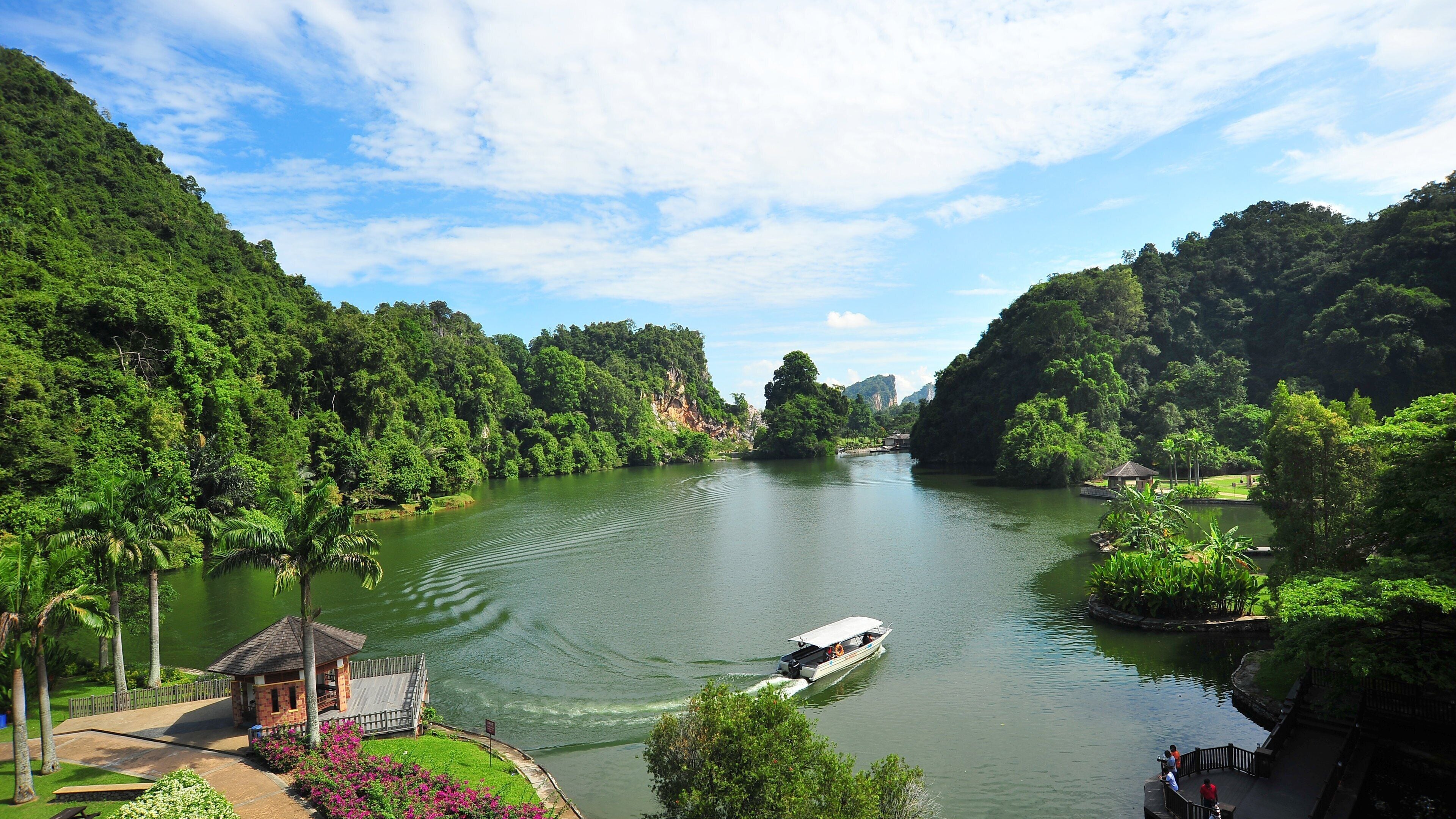 A river surrounded by lush greenery and hills. A boat is seen on the water.