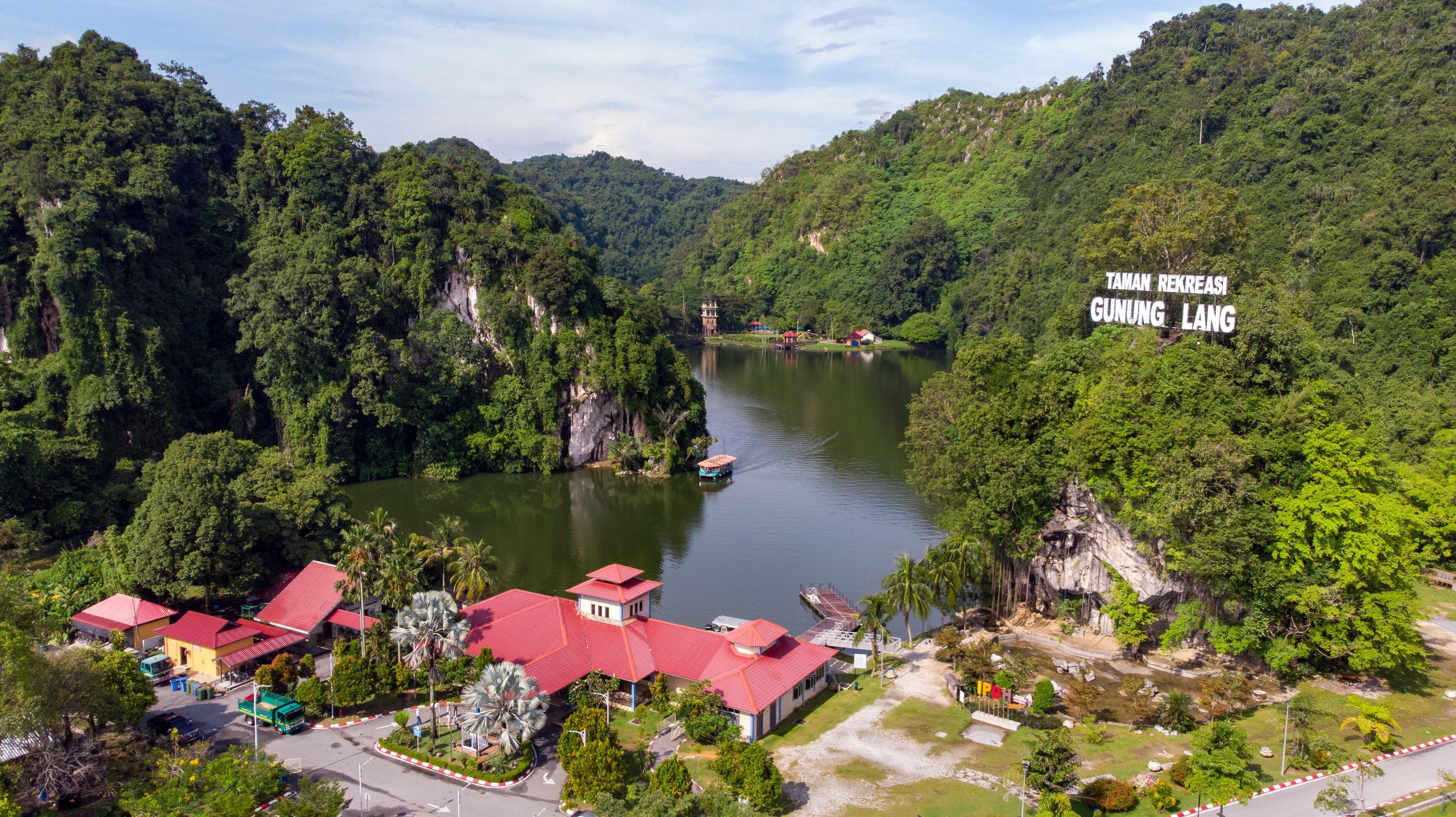 A river surrounded by lush green hills, a boat, and a building with a red roof.