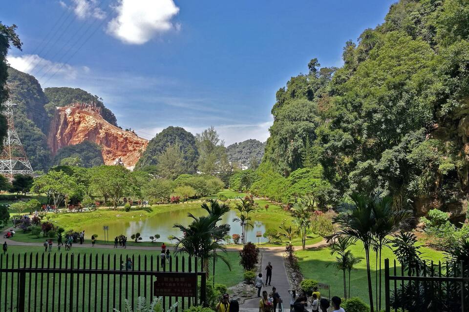 A park with a pond, lush greenery, and rocky cliffs.