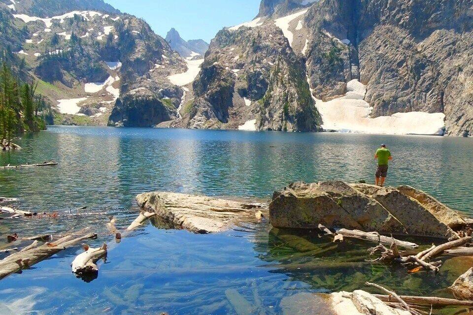 A clear mountain lake with rocky shores and a person standing on a rock.