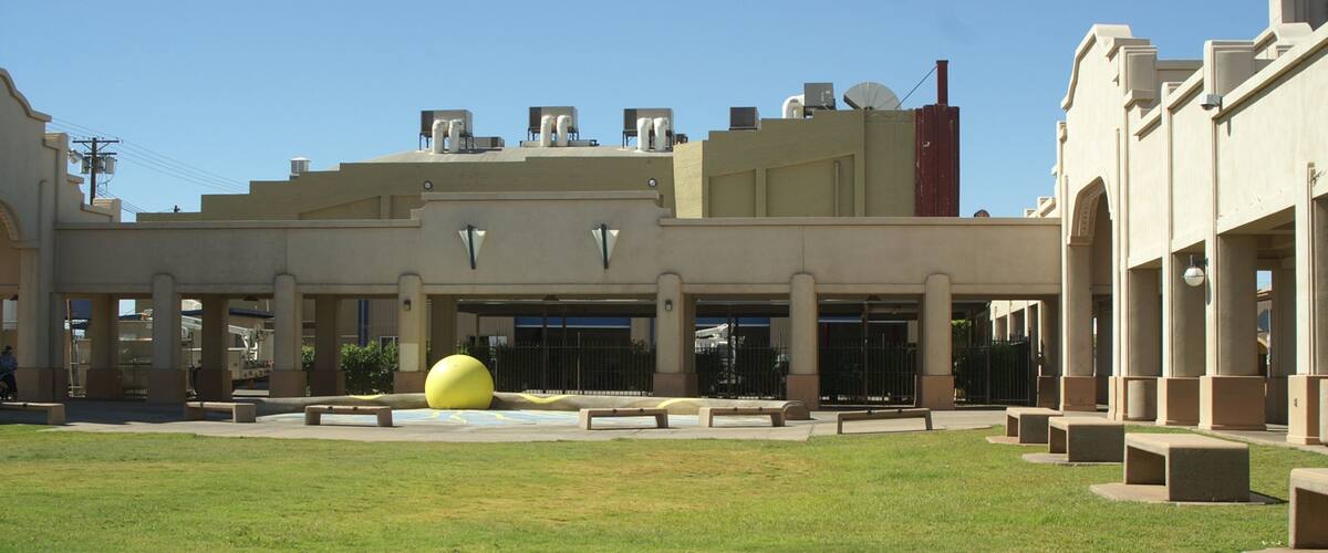 A courtyard with a large yellow sphere, a building with a flat roof, and a clear blue sky.