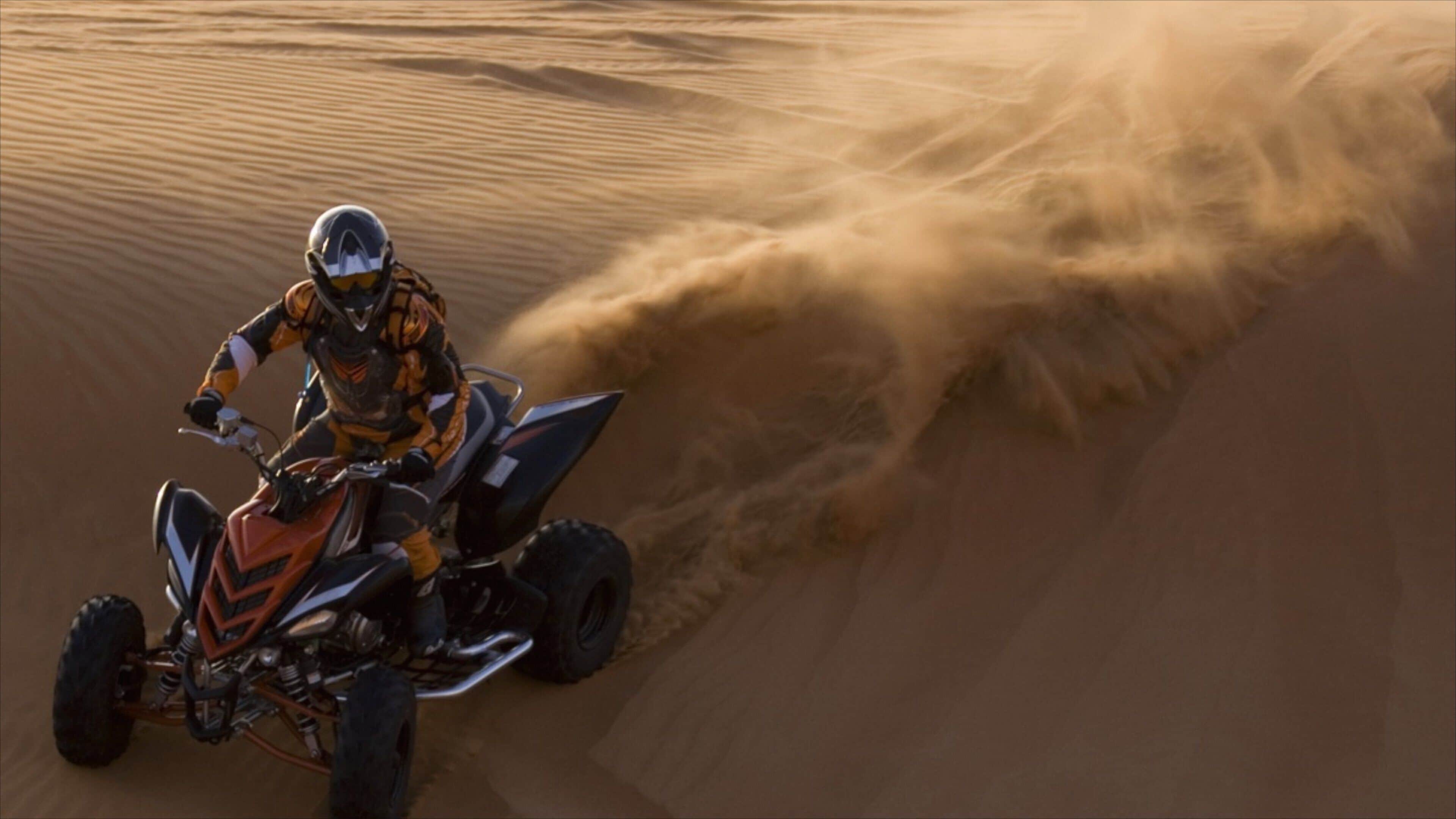 A person riding a quad bike on a sandy dune.