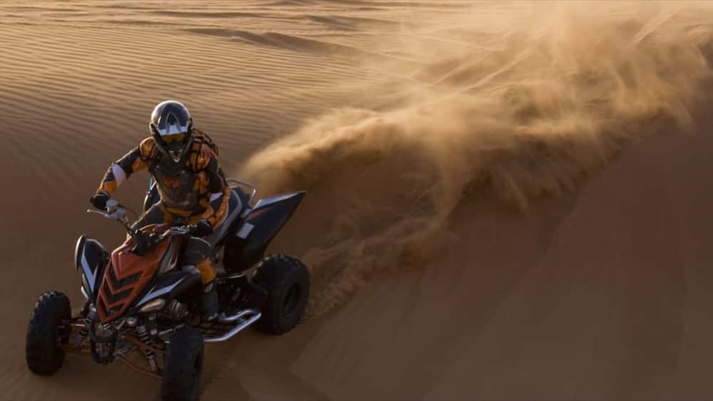 Une personne conduisant un quad sur une dune de sable.