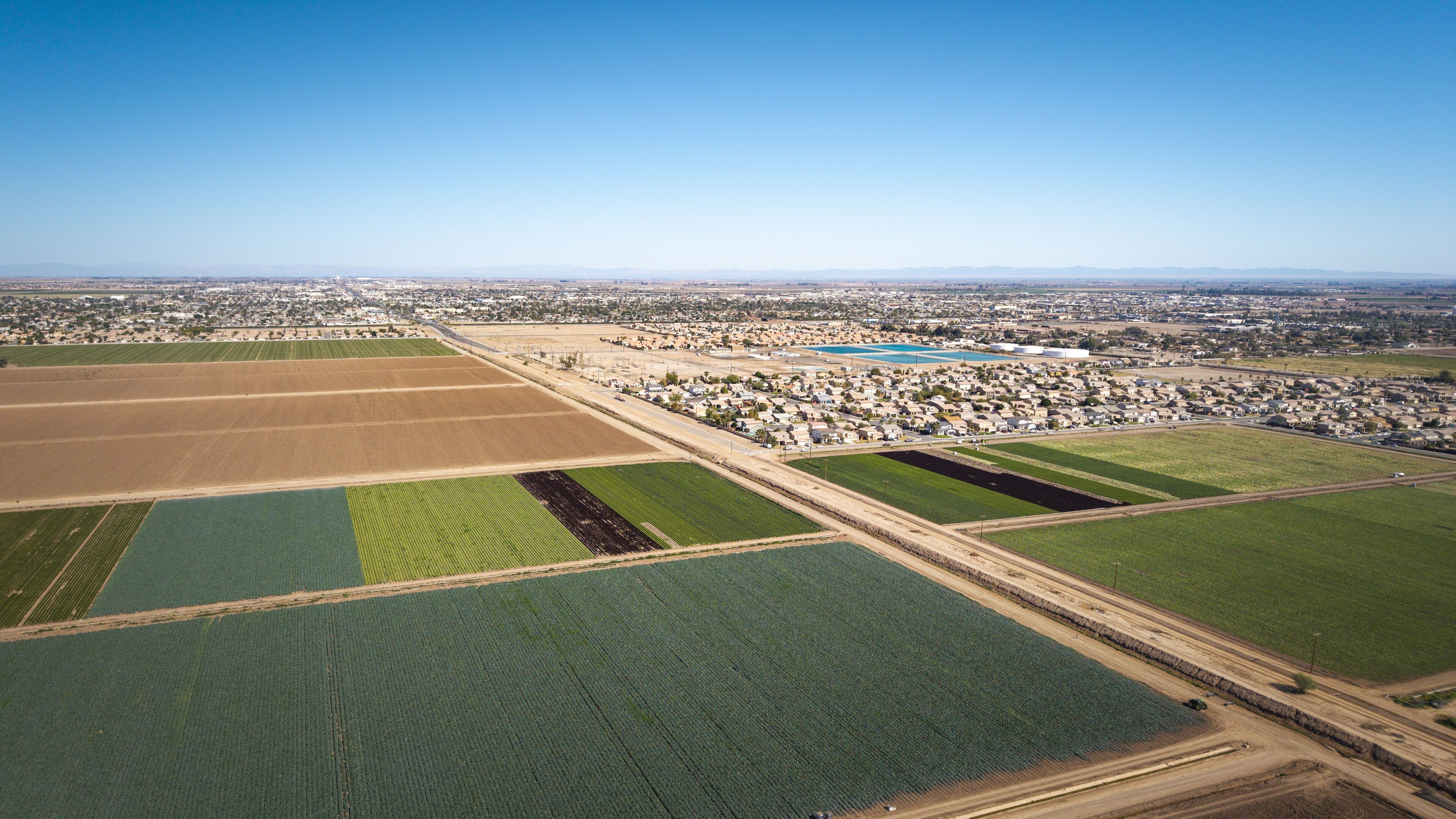 Aerial view of the sprawling green and brown fields meeting the city's edge under a boundless sky, El Centro, California, United States.
