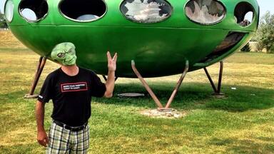 A green UFO-like structure with multiple circular openings and a person standing in front of it.