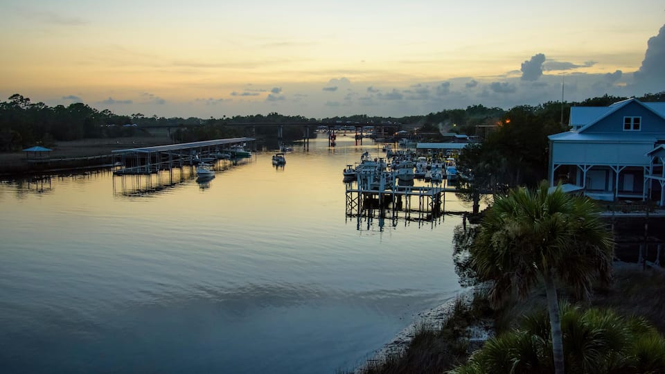 A marina with boats docked, a pier, and a house by the water during sunset.