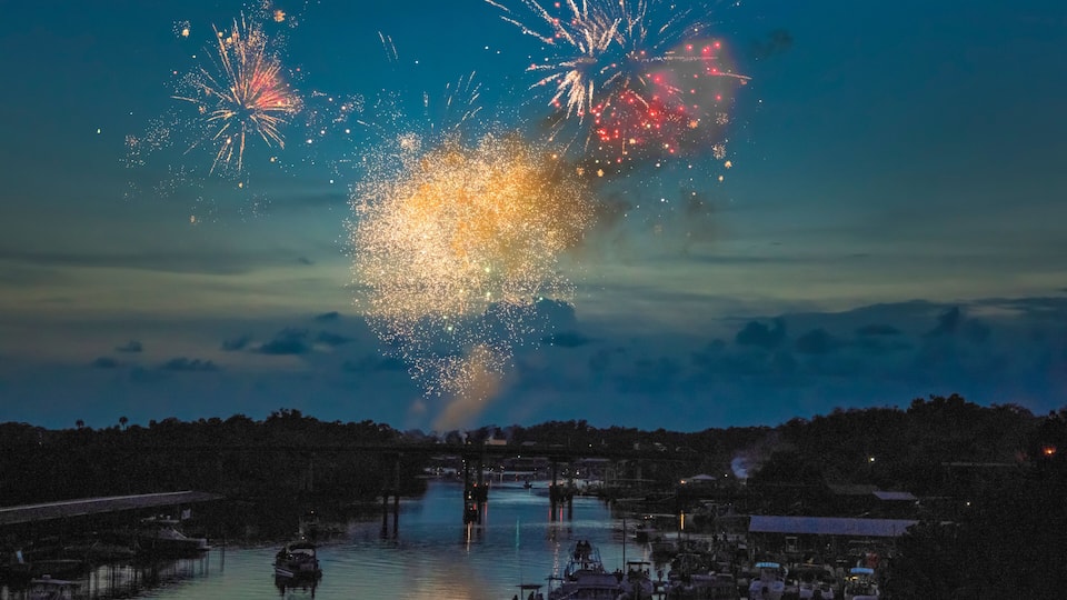 Fireworks over a river with boats and a bridge.