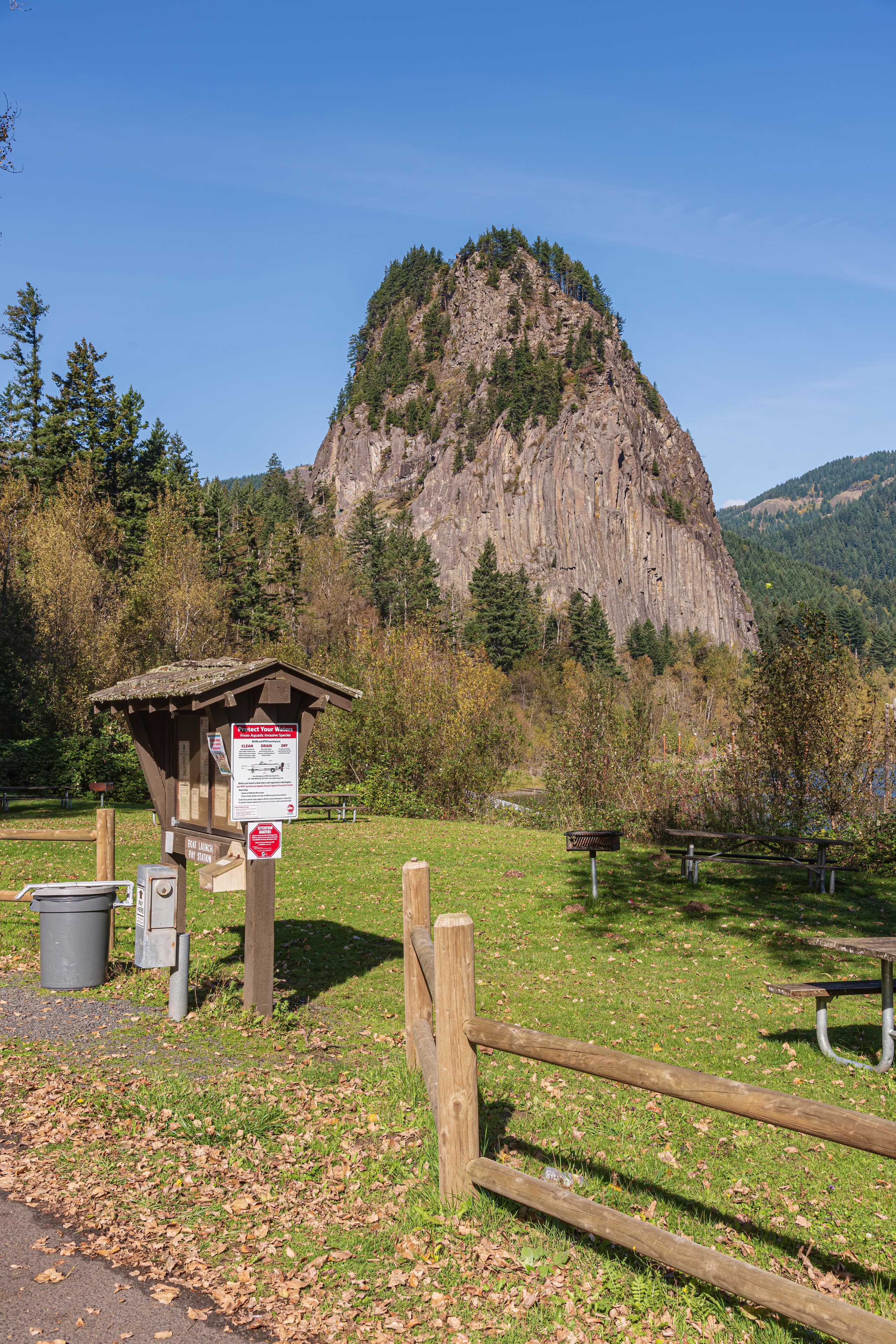 A picnic area with a wooden bench, a trash can, and a signpost with information.