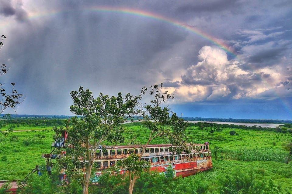 A red boat on a river with a rainbow in the sky.